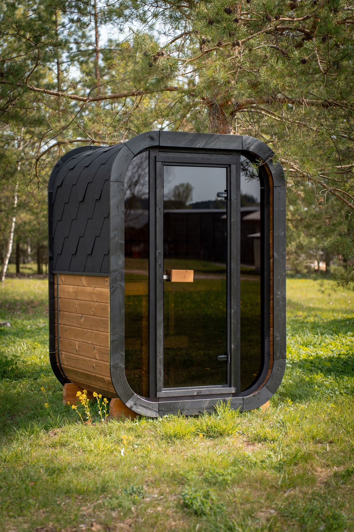 Two-seater Nordic pine cube sauna with a full glass front in a garden